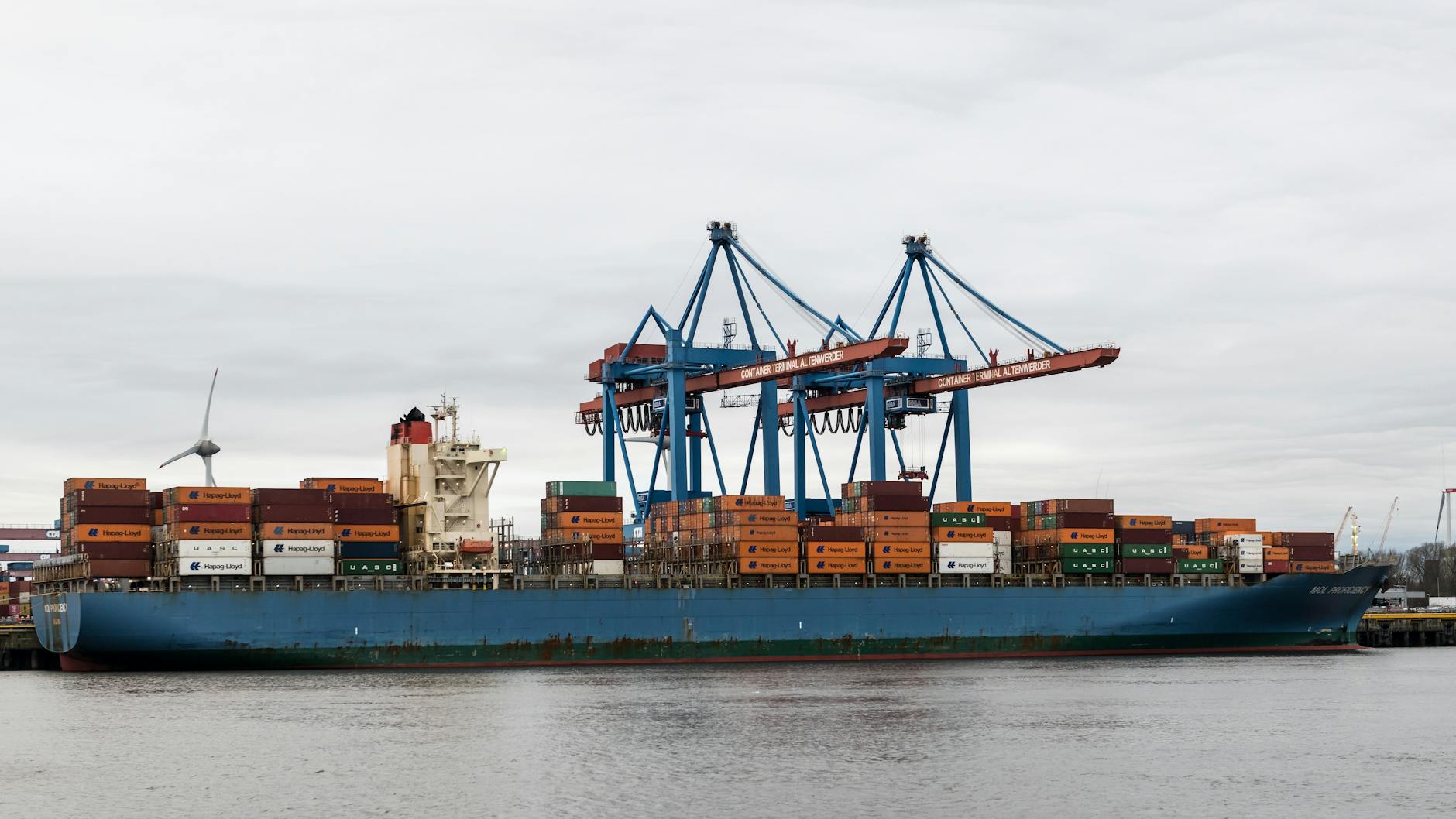 A container ship docked at Hamburg port surrounded by cranes and shipping containers.